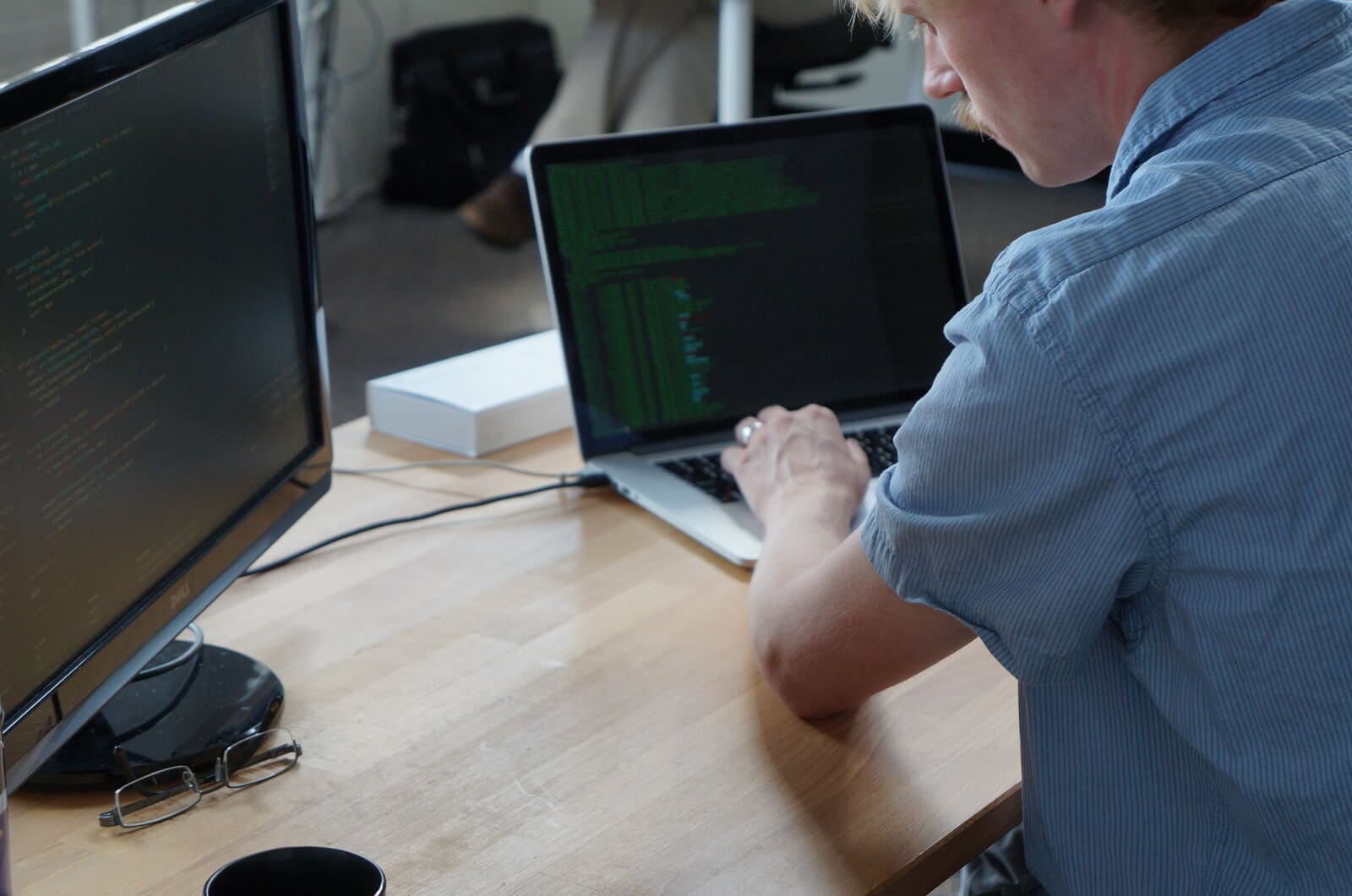 Developer working across a laptop terminal and a second monitor running a code editor