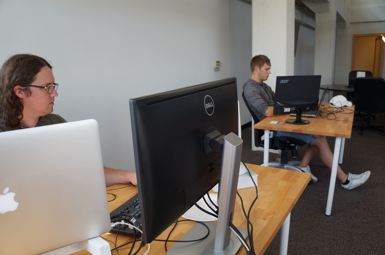 Two developers working at laptops and desktop monitors in a shared studio space