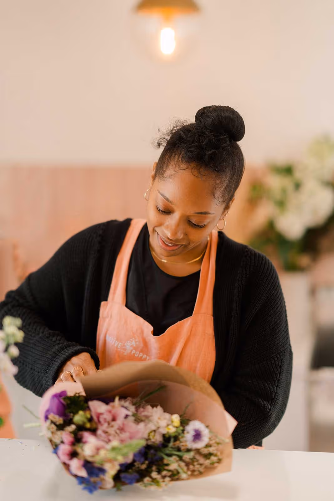 A female florist arranging a flower bouquet and wrapping it in branded paper. 