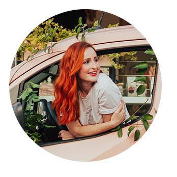 A woman with red hair leaning out of a window of a pink flower delivery van