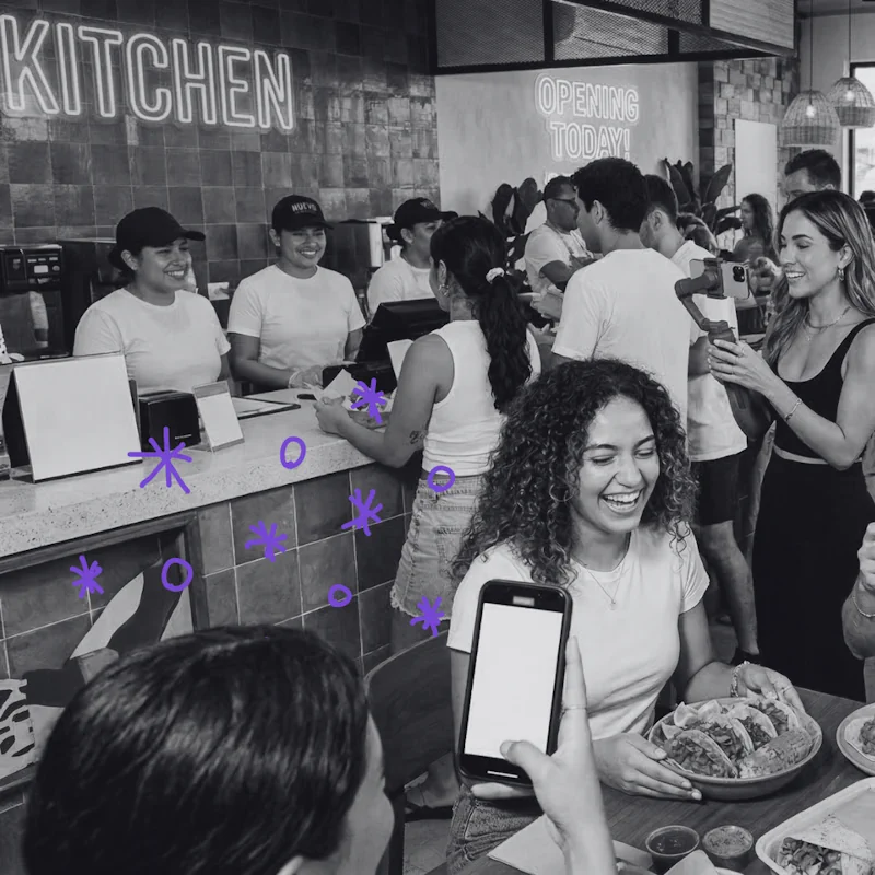 A busy restaurant "Kitchen" with staff smiling and an influencer using a gimbal to film food, showcasing successful QSR PR results.