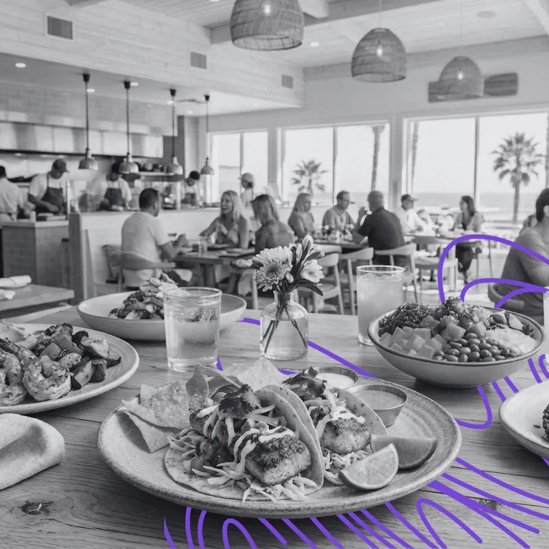 Gourmet tacos and healthy bowls on a dining table at a crowded coastal fast-casual restaurant, highlighting restaurant marketing challenges