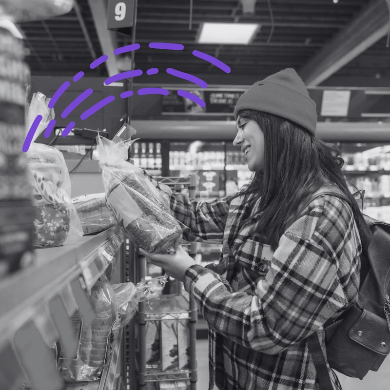 Happy shopper selecting a loaf of packaged bread from a grocery store shelf, illustrating increased brand awareness and retail sales.