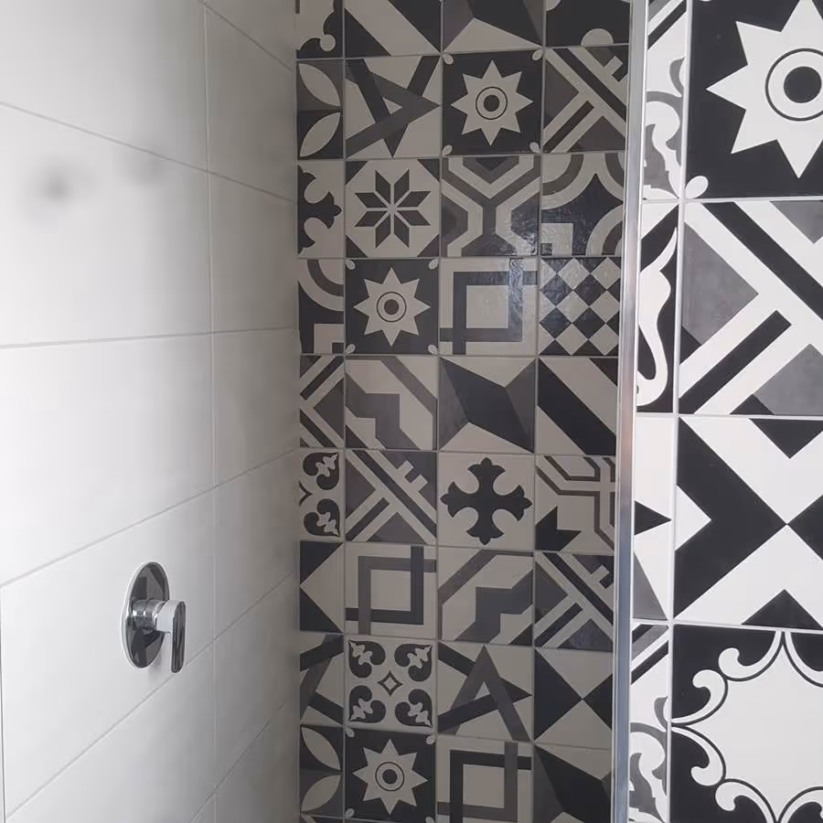 Shower wall with white tiles on one side and patterned black and gray geometric tiles with various shapes on the other side.