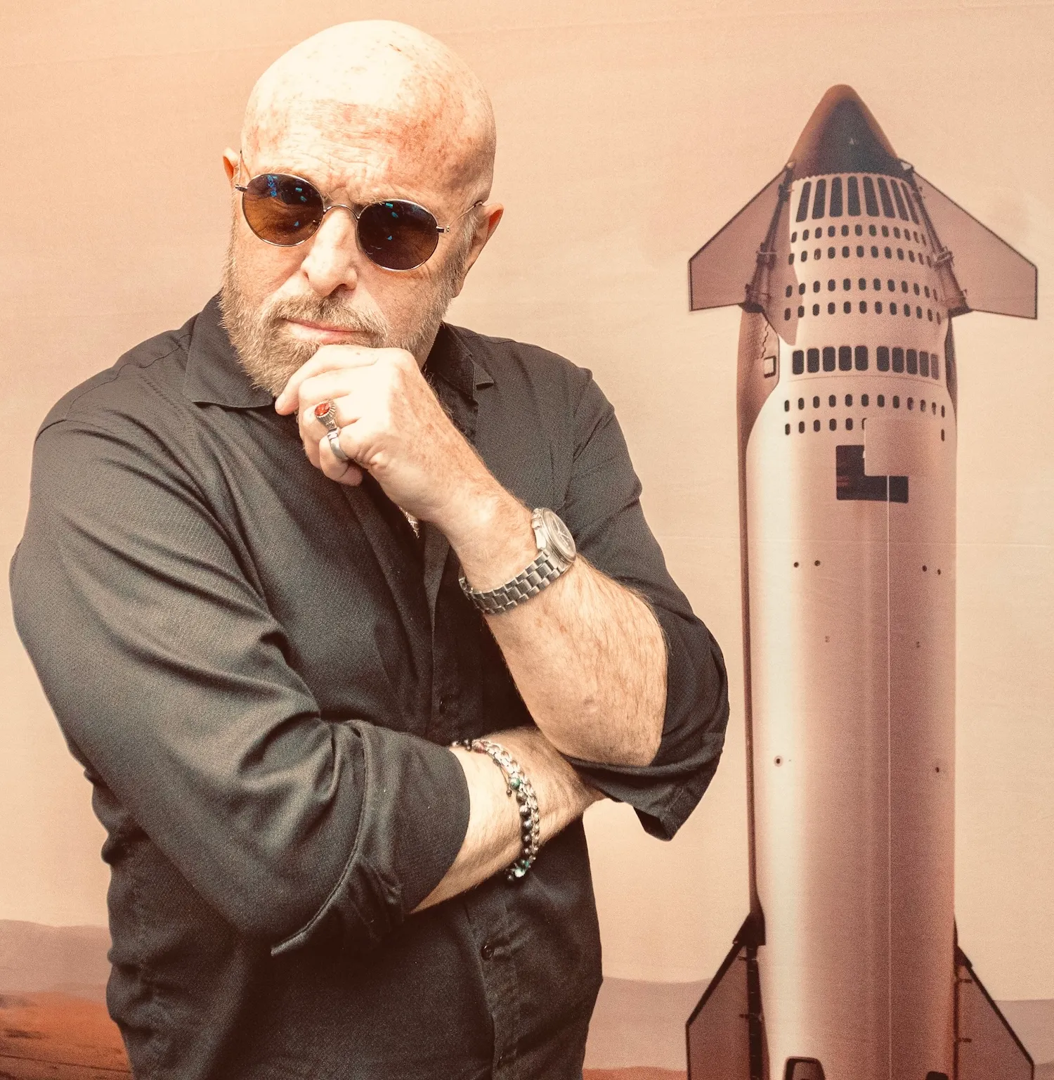 Bald man in sunglasses posing thoughtfully next to a rocket