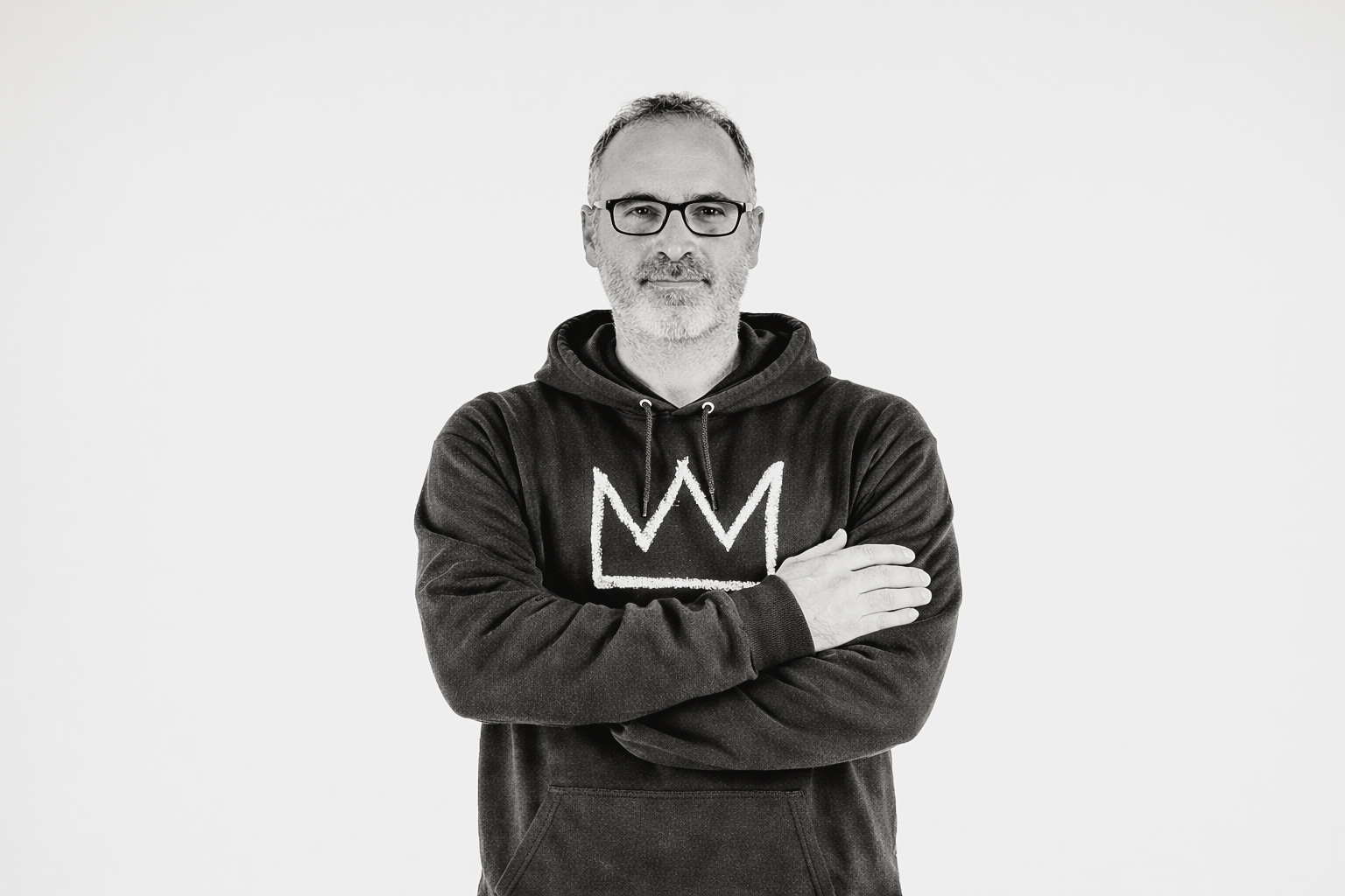 Man with glasses wearing black hoodie with crown logo, arms crossed