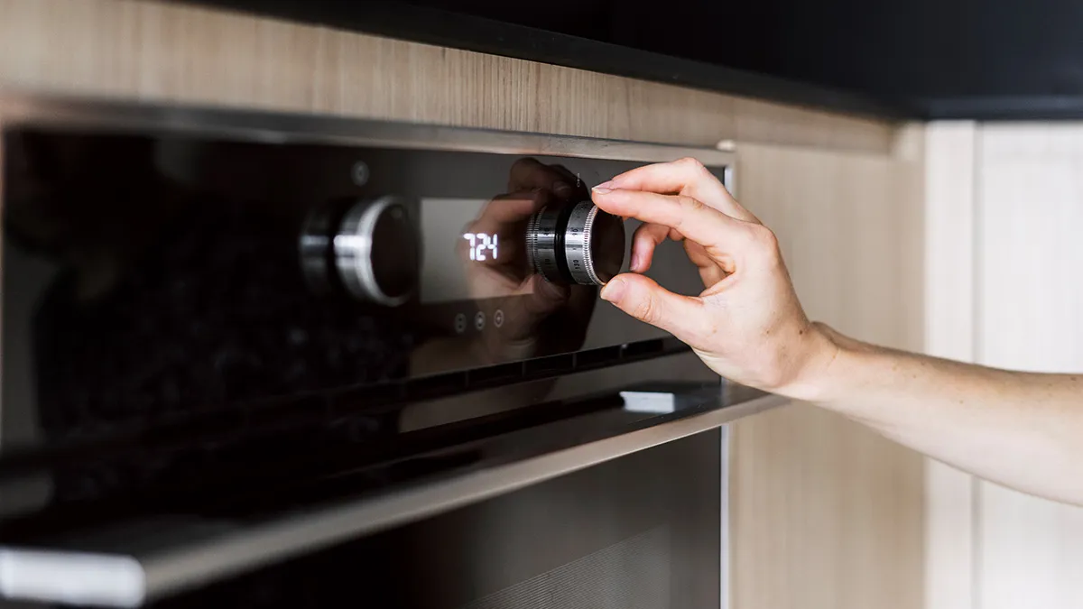 Hand adjusting the dial on a modern built-in oven with a digital display showing the time 7:24.