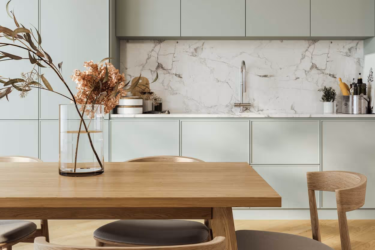 Modernt kök med ljusgröna skåp, marmorbänkskiva och träbord med vas och torkade blommor.
