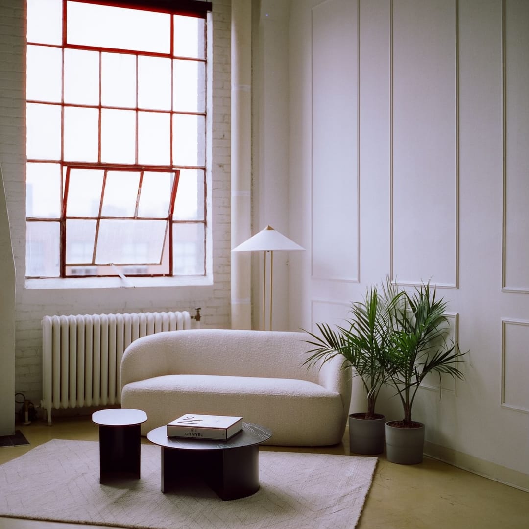 Curved cream sofa, palms and panelled white walls lit by a tall west-facing window