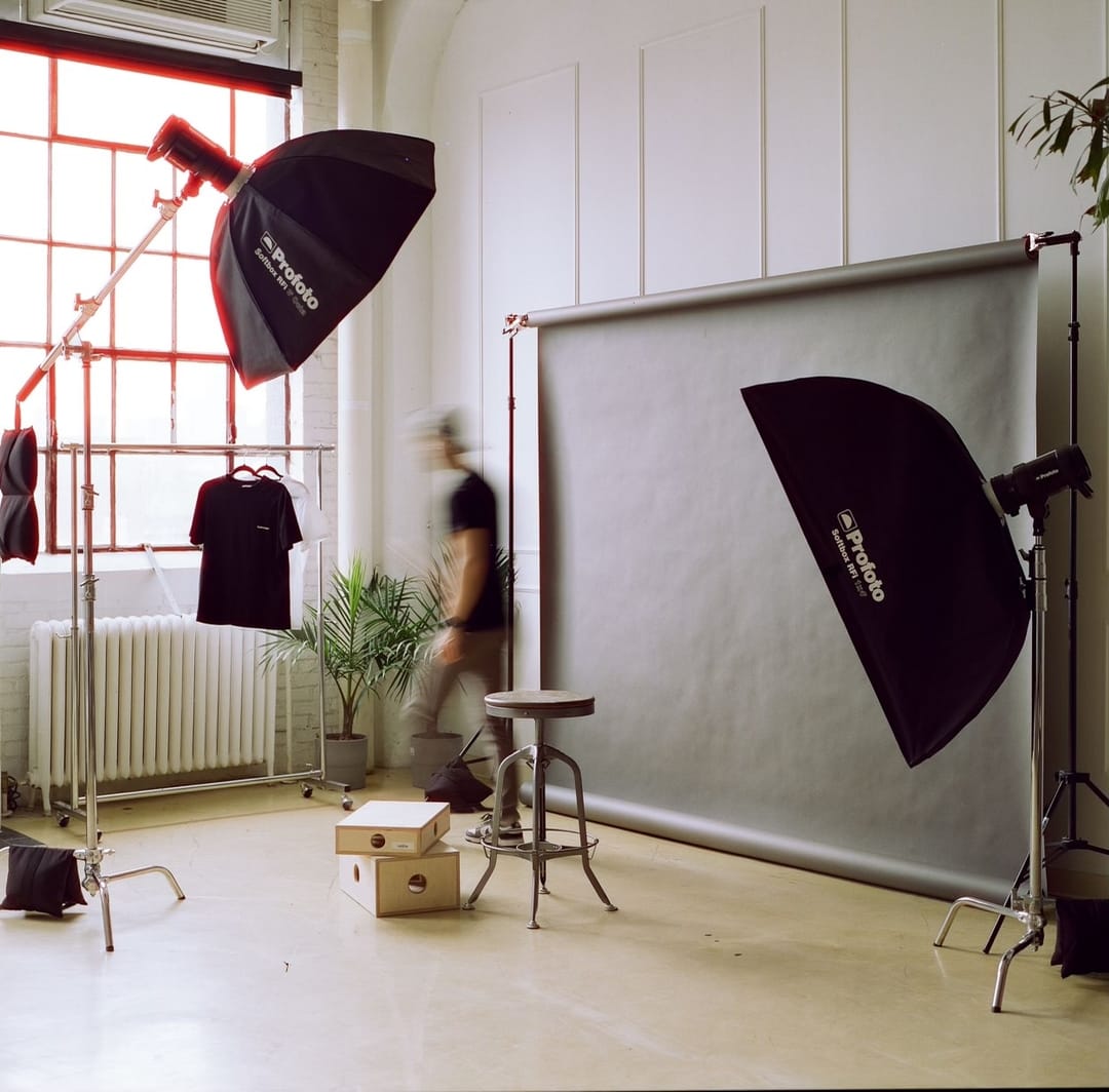 Photographer moving between softboxes and a grey seamless backdrop during a studio shoot
