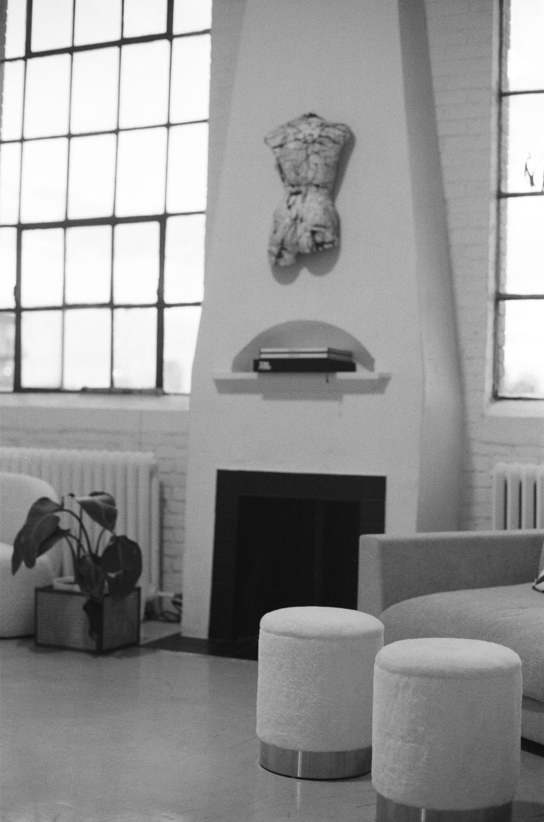 Black-and-white photo of the white fireplace with a plaster sculpture and ottomans