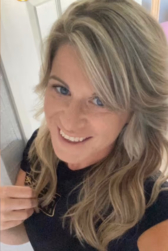 Smiling person with long, wavy hair wearing a black shirt, looking up at the camera.