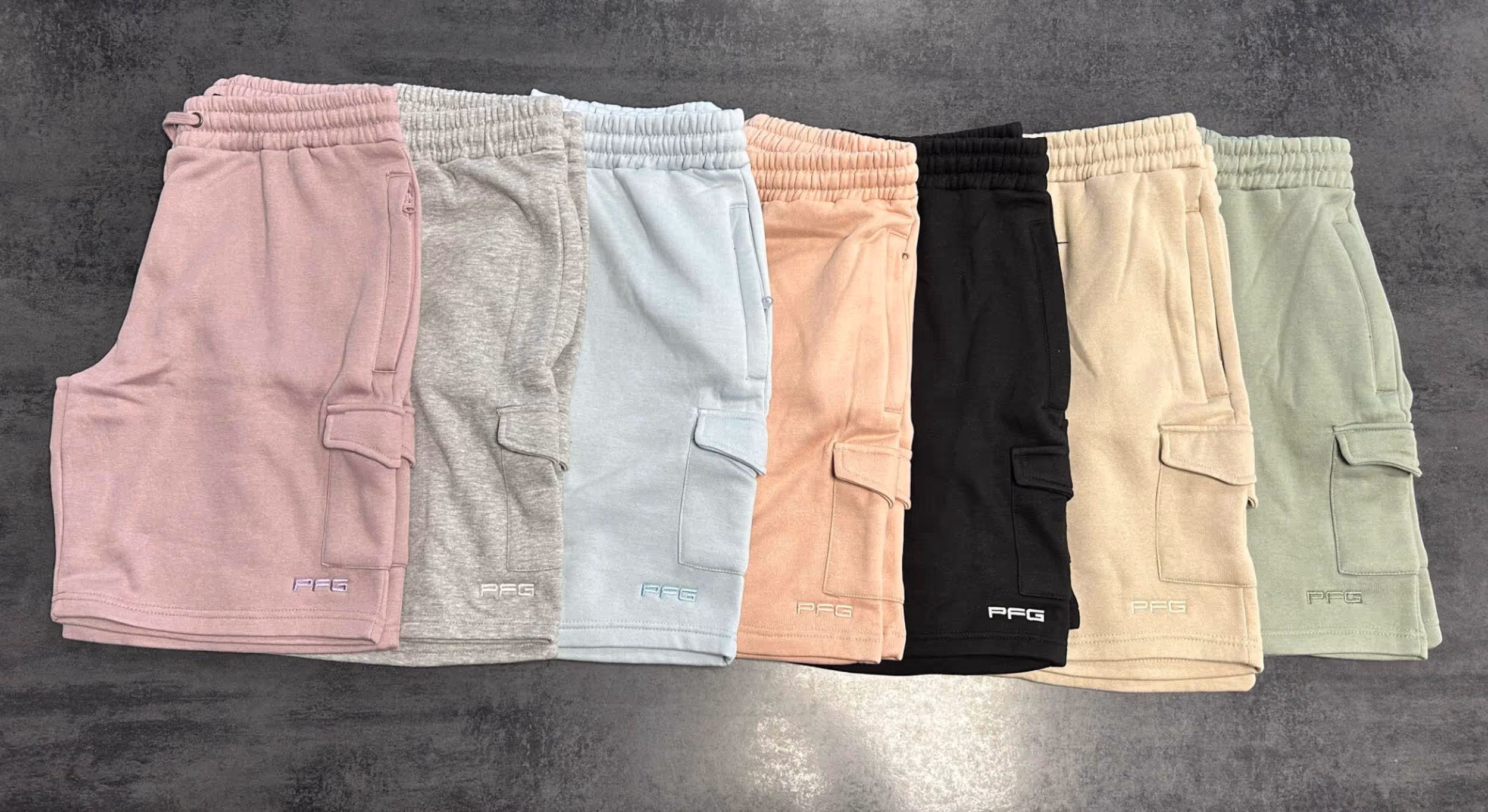 Seven pairs of shorts in pink, gray, blue, peach, black, beige, and green displayed in a row.