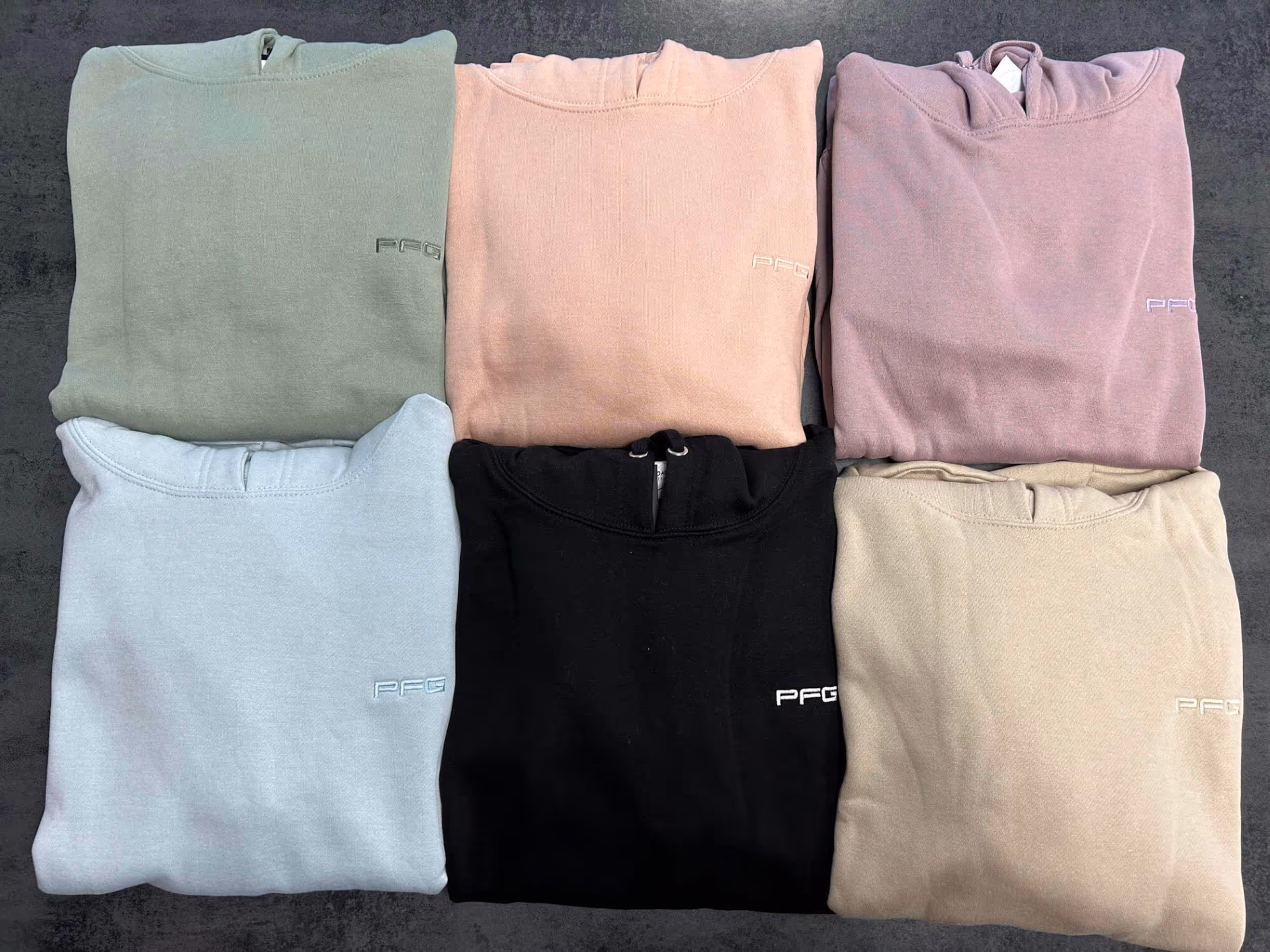 Six folded sweatshirts in pastel and neutral colors arranged in two rows on a dark surface.
