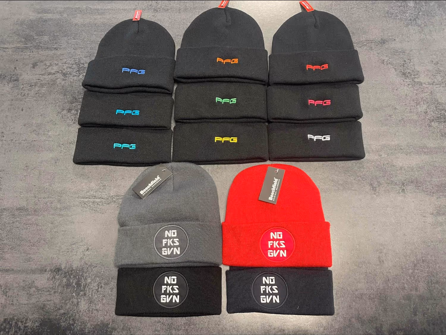 Rows of black, gray, and red beanies with different logos displayed on a flat surface.