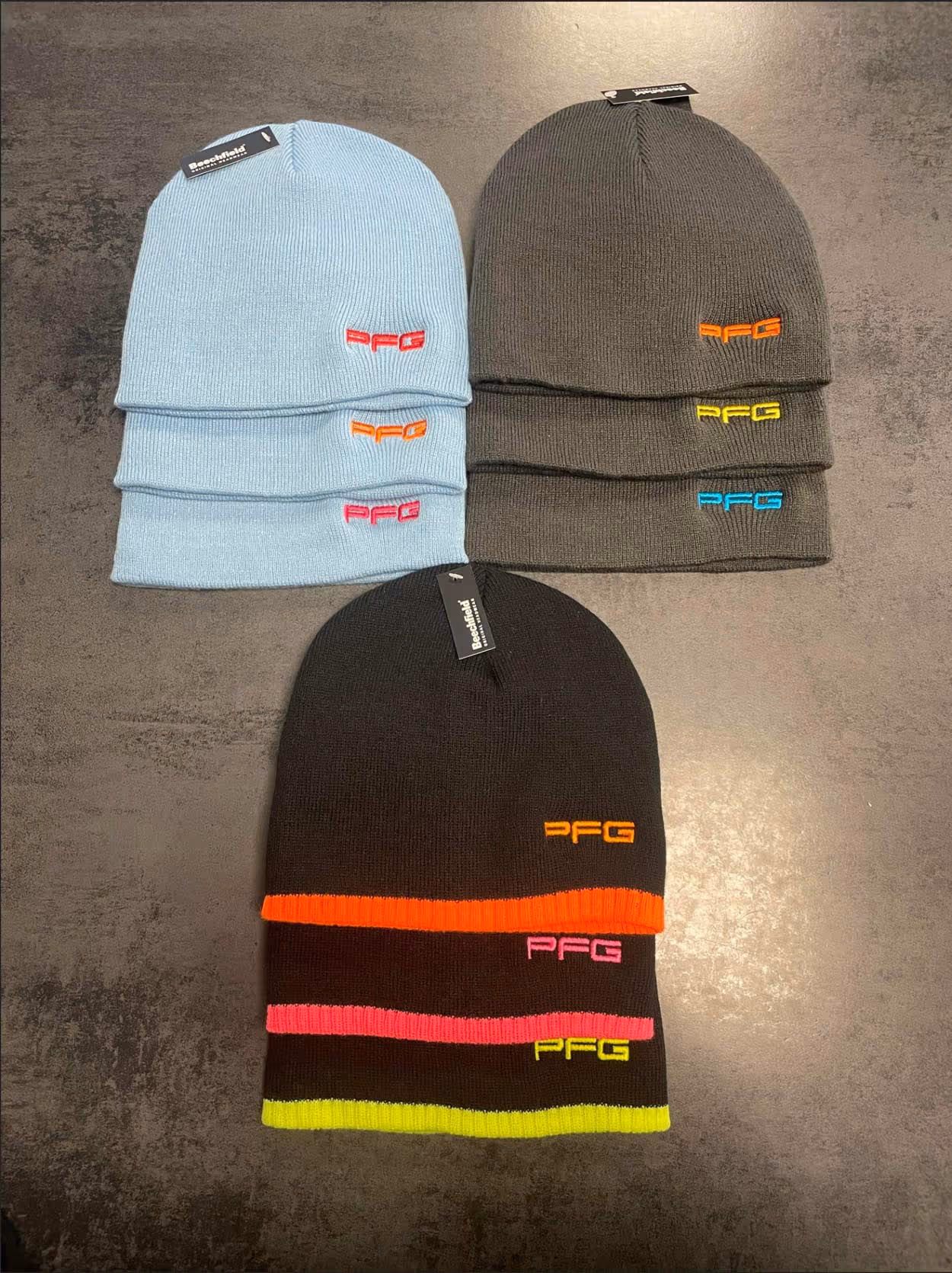 Eight beanies in different colors with small embroidered logos displayed on a dark surface.