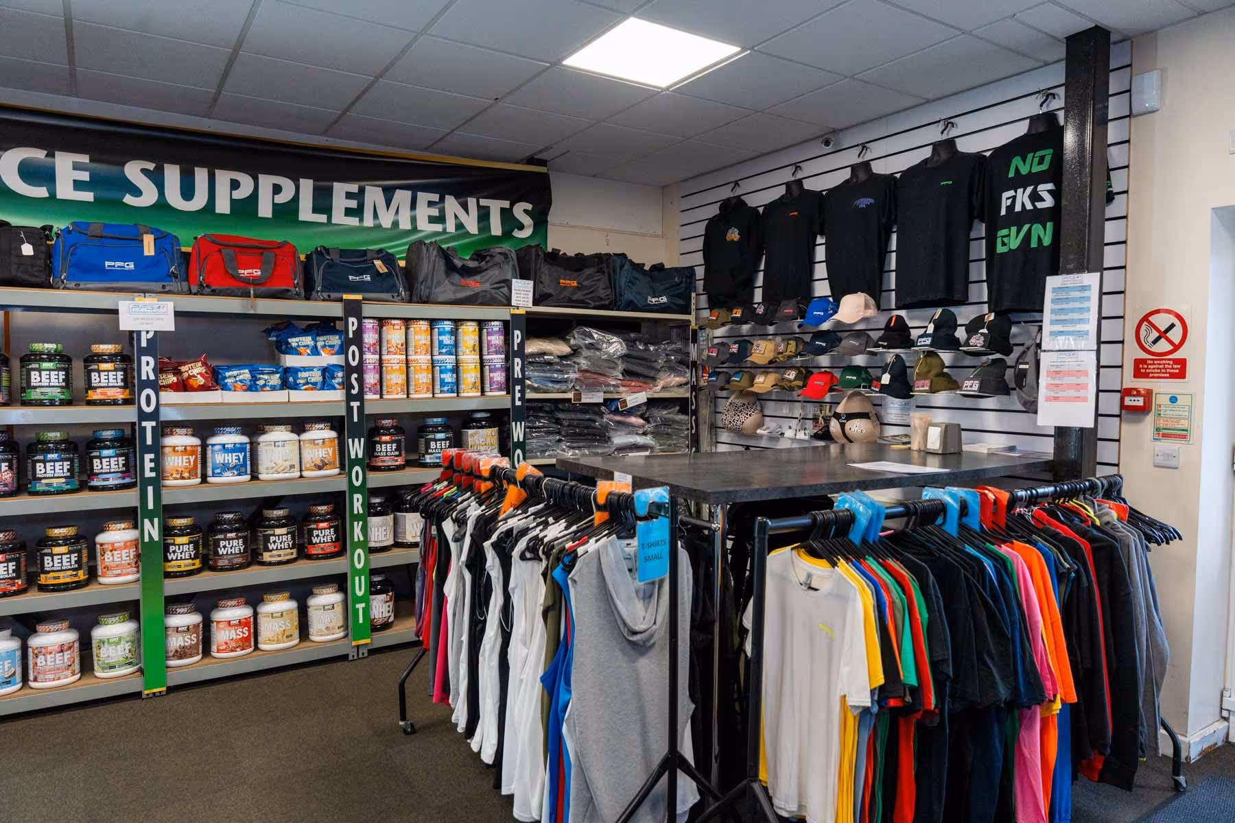 Clothing and supplement store display with shirts on racks and shelves stocked with various supplement containers.