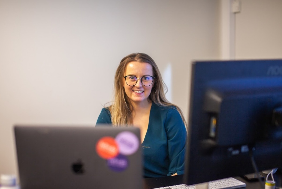 Kvinne ved kontorpulten sin som smiler til kamera