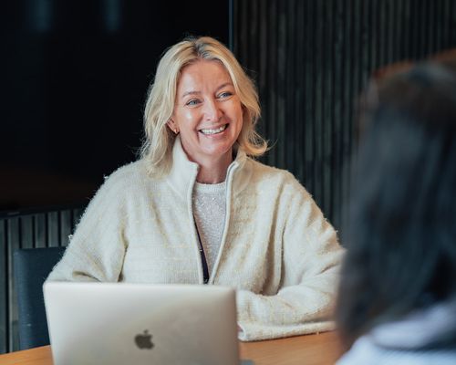 Smilende kvinne som sitter foran en mac