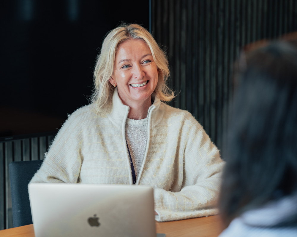 Smilende kvinne som sitter foran en mac