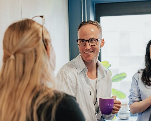 Mann med lilla kaffekopp smiler mot kvinne