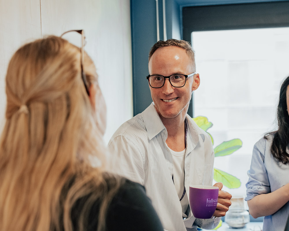 Mann med lilla kaffekopp smiler mot kvinne