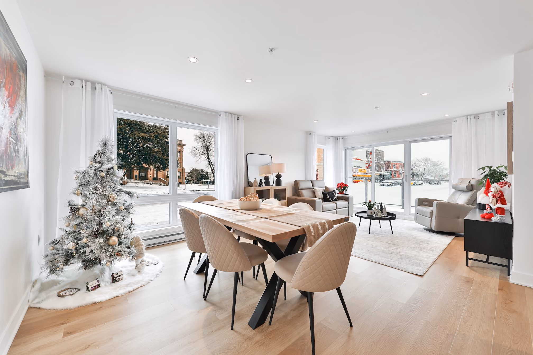 Bright modern living and dining area with Christmas tree, large windows, beige chairs, and leather recliners.