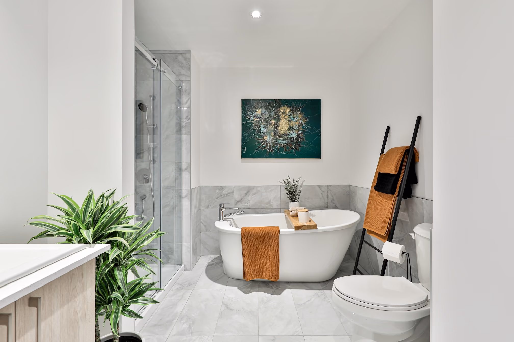 Modern bathroom with freestanding tub, glass shower, toilet, plant, and orange towels on ladder rack.