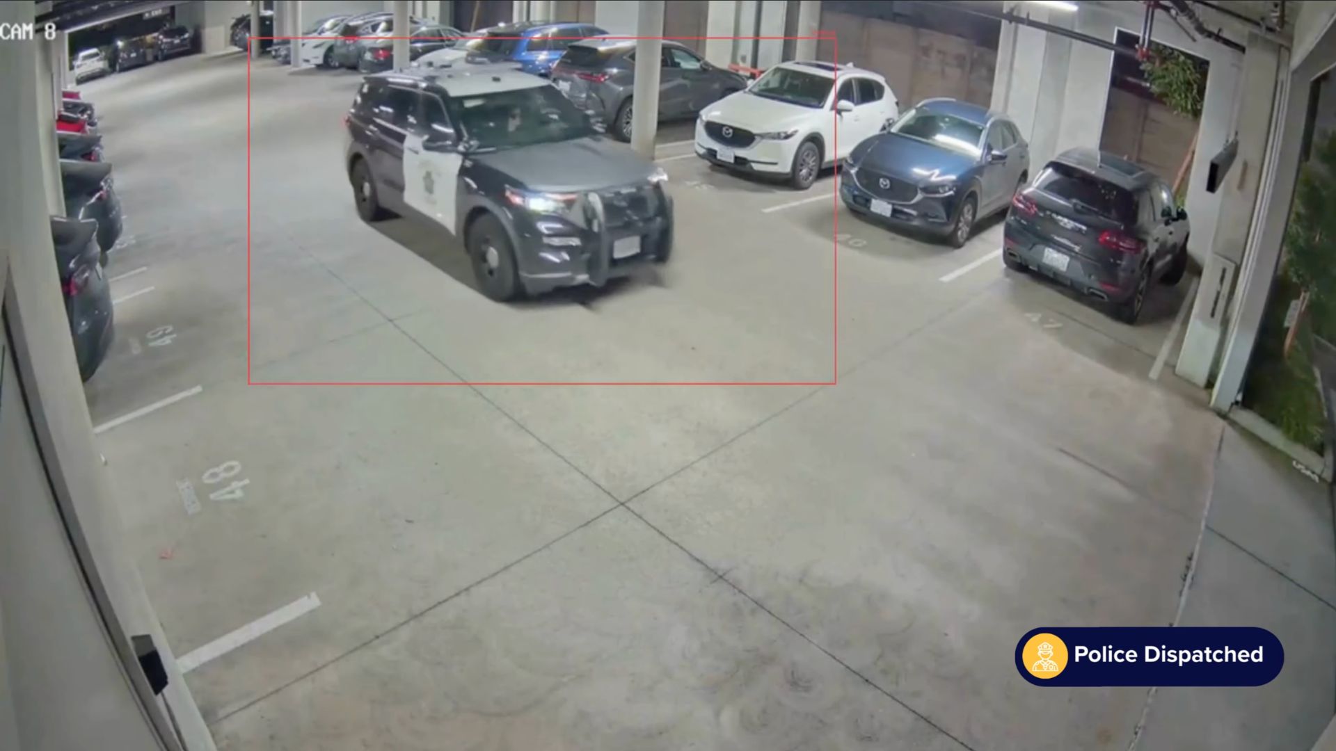 Black and white police SUV driving inside a parking garage next to parked cars.