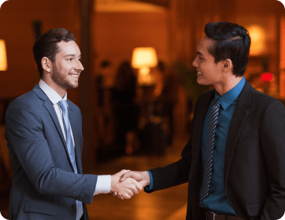 Two businessmen smiling and shaking hands in a warmly lit indoor setting.