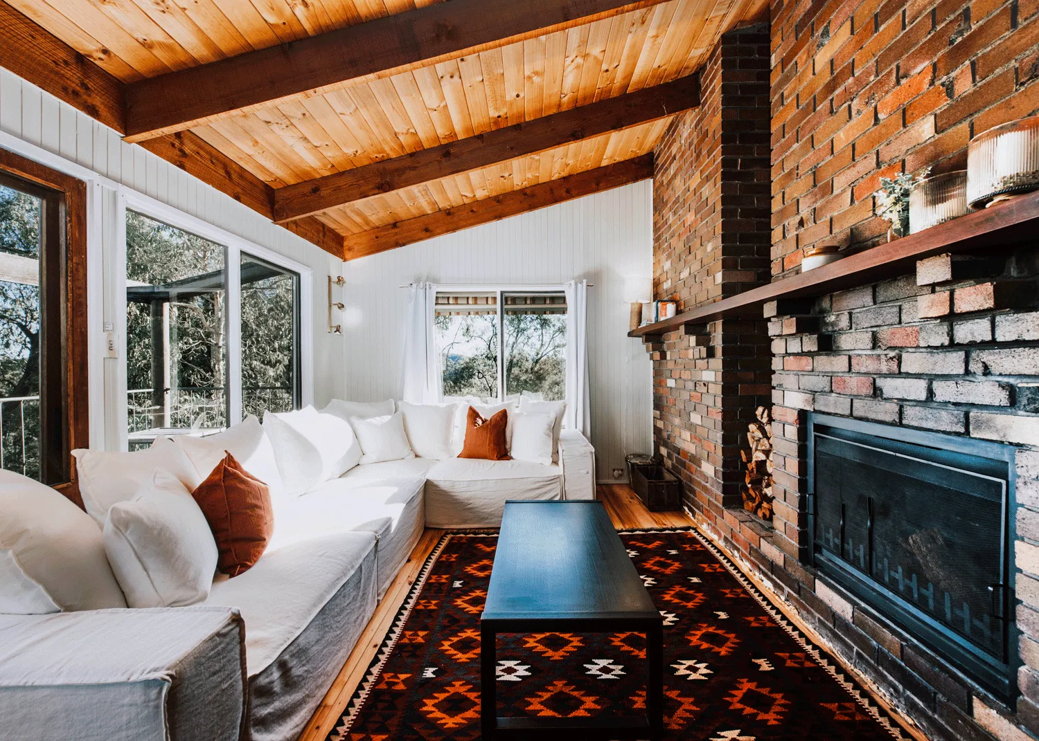 A white L-shaped couch in front of a black coffee table and a fireplace in the living room of Ilkley House: A Refreshing Family Rural Getaway, an Airbnb in Mudgee