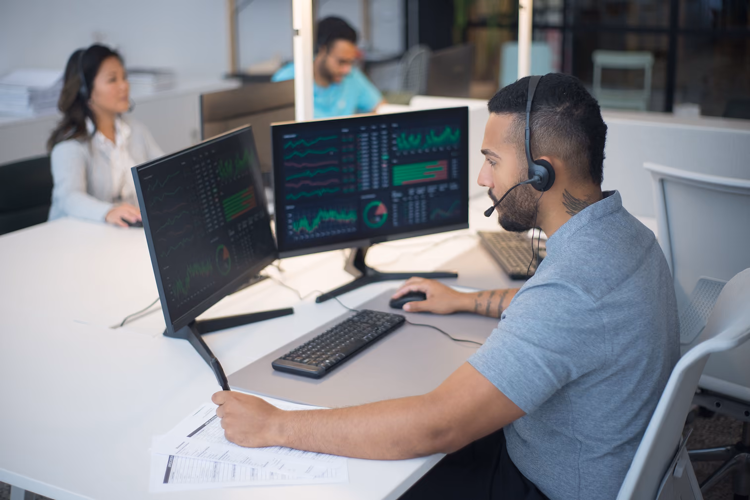 Man with headset working at desk with dual monitors showing data charts and graphs.