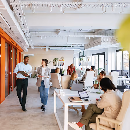 People collaborating and working in a modern, bright open office space with laptops and documents.
