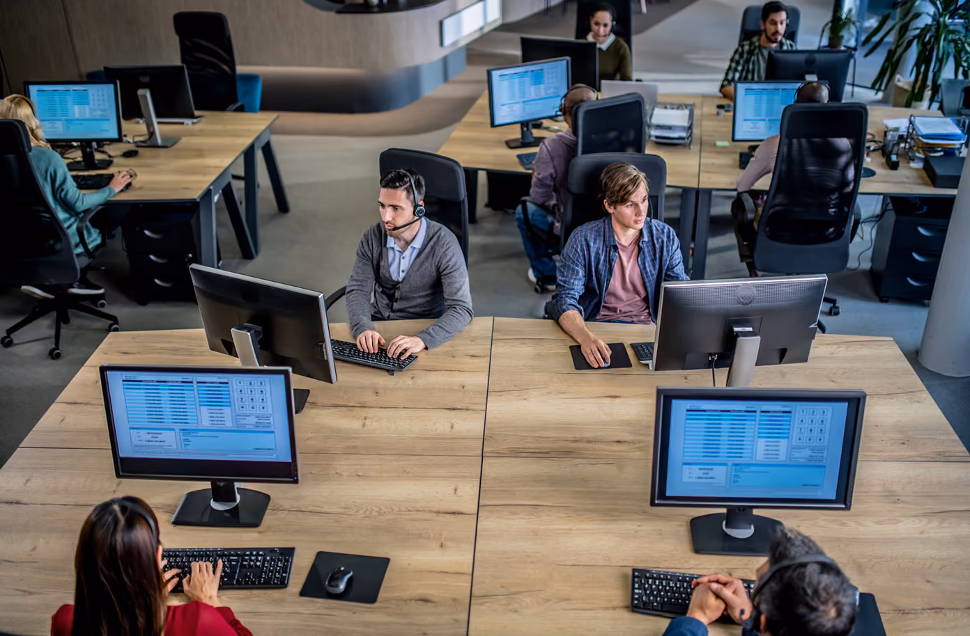 Call center workers at desks using computers and headsets in a modern office space.