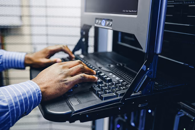 Close-up of hands typing on a keyboard attached to a server rack console in a data center.