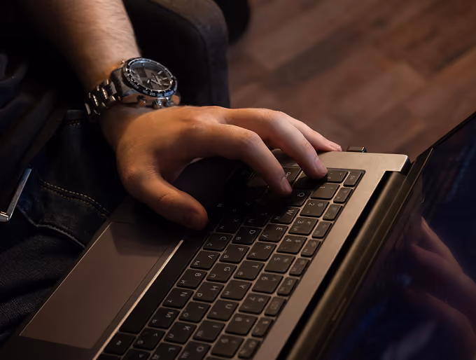 Person typing on a laptop keyboard wearing a silver wristwatch with a black face.