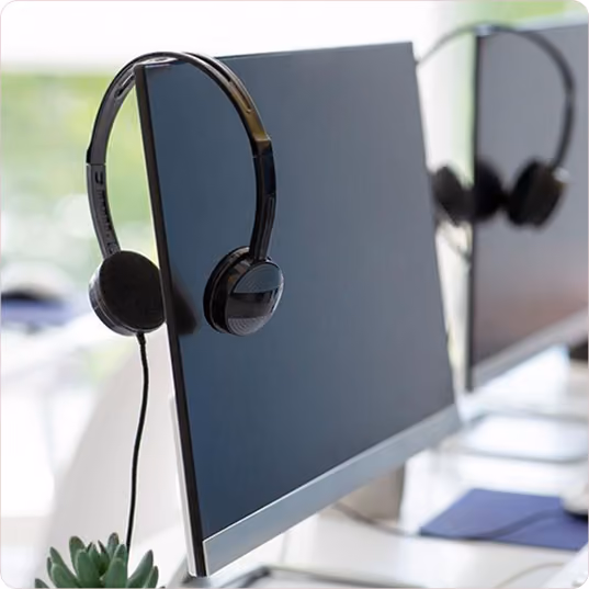 Black headset hanging on the corner of a turned-off desktop computer monitor in an office setting.