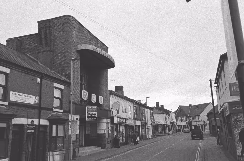 A black and white photograph of Church Street, a shopping street in Coalville, England, including the disused Rex cinema building closed in 1984.