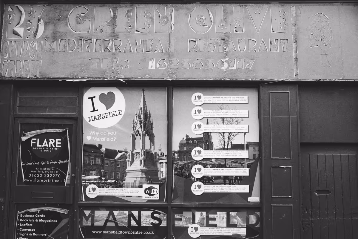 A disused restaurant shop front on Church Street, Mansfield, featuring the traces of the removed lettering "23 Church Street, Green Olive Mediterranean Restaurant" and stickers which read "I heart Mansfield".