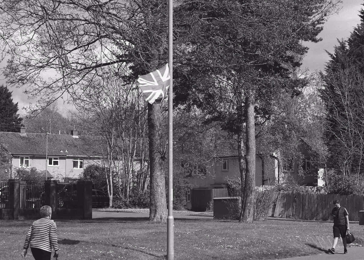 A black and white photo of a residential street in Corby, England, featuring a Union Jack flag tied to a lamppost.