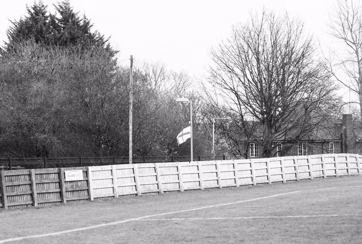 A black and white photo of a football field and back alley in Mansfield, England, featuring an English flag tied to a lamppost.