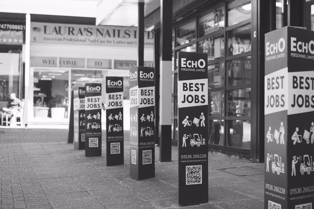 The exterior of Echo Personnel recruitment offices in Corby, England. Signage reads "Echo Personnel, best jobs" and includes icons of workers lifting boxes and using factory vehicles.