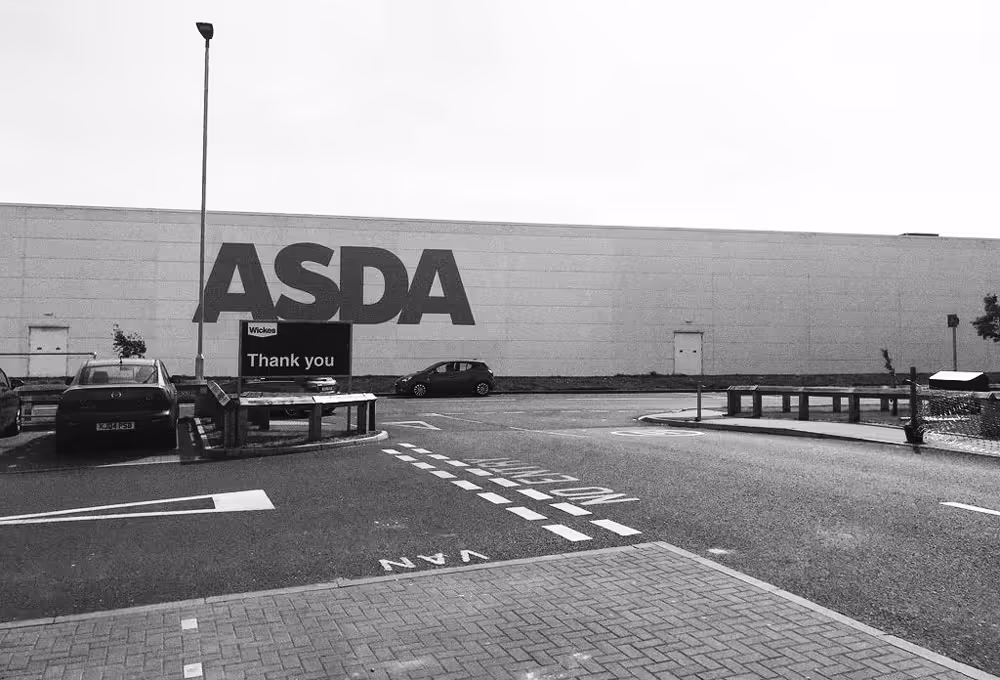 A black and white photo of a big Asda superstore building and car park in Peel Retail Park, Corby, England.