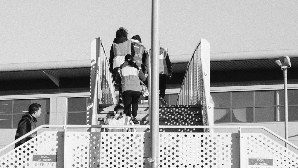 A black and white photo of a factory in Mansfield, England, with workers in high vis jackets climbing the stairs to enter.