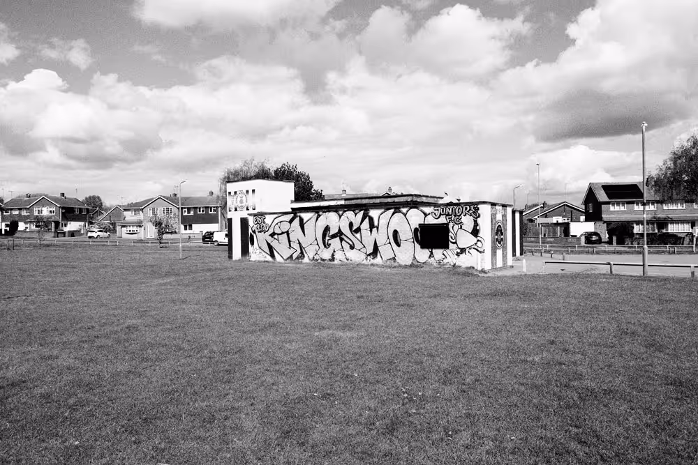 A black and white photo of the Kingswood Estate in Corby, featuring a row of bins for collection and purpose built houses and flats.