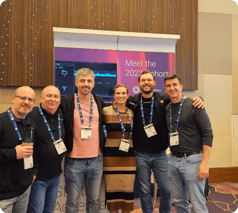 Group of six people posing together in front of a conference banner with event badges around their necks.