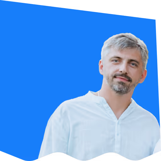 Man with gray hair and beard wearing a white shirt against a blue geometric background.