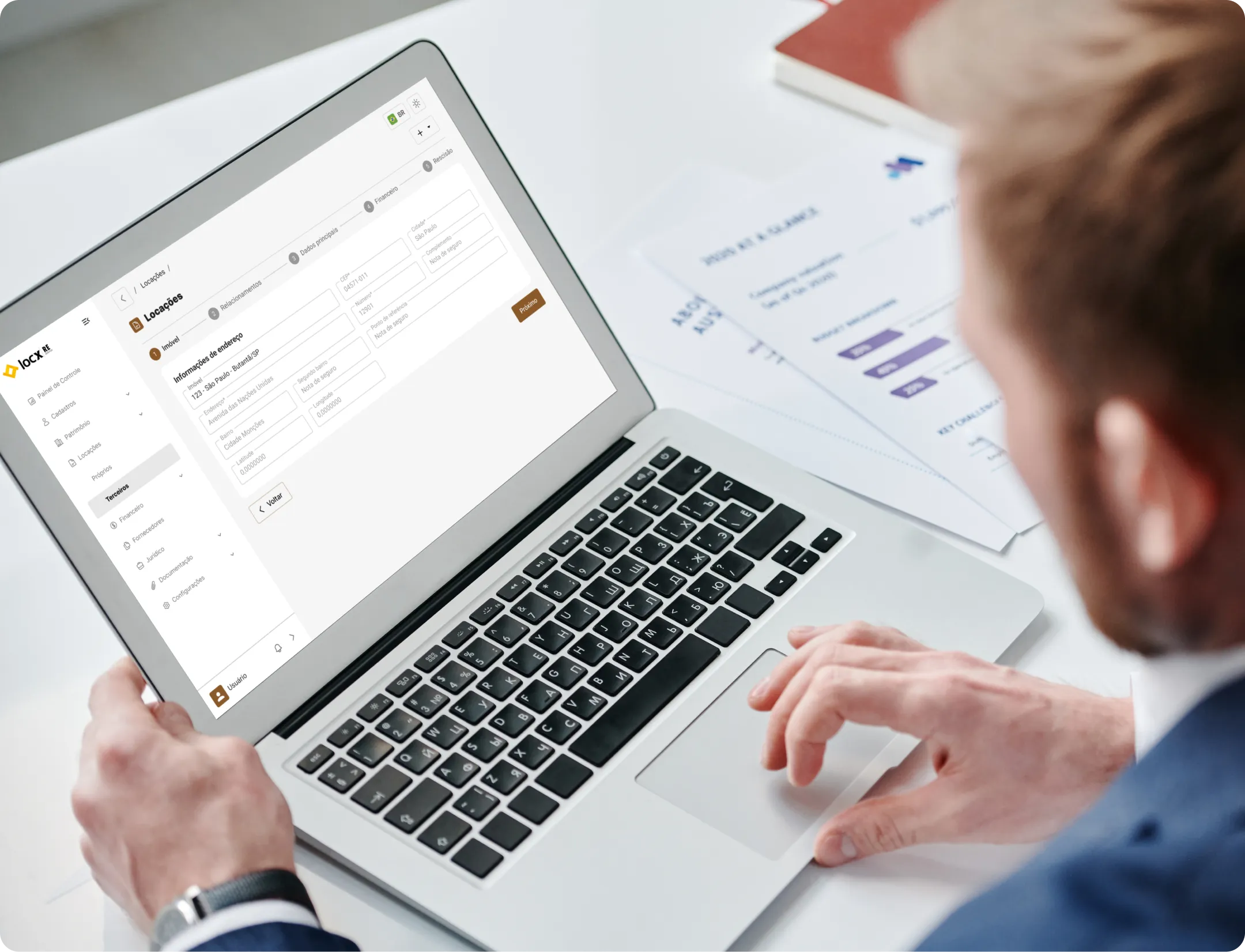 Pessoa usando laptop com software de cadastro imobiliário aberto, exibindo formulário de informações de endereço.