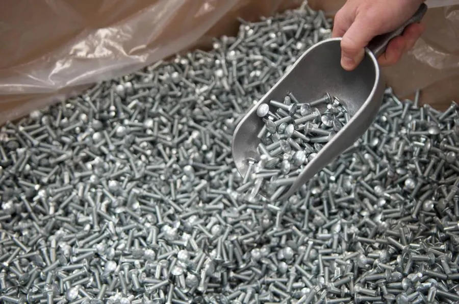 Scoop lifting metal bolts from a bulk container