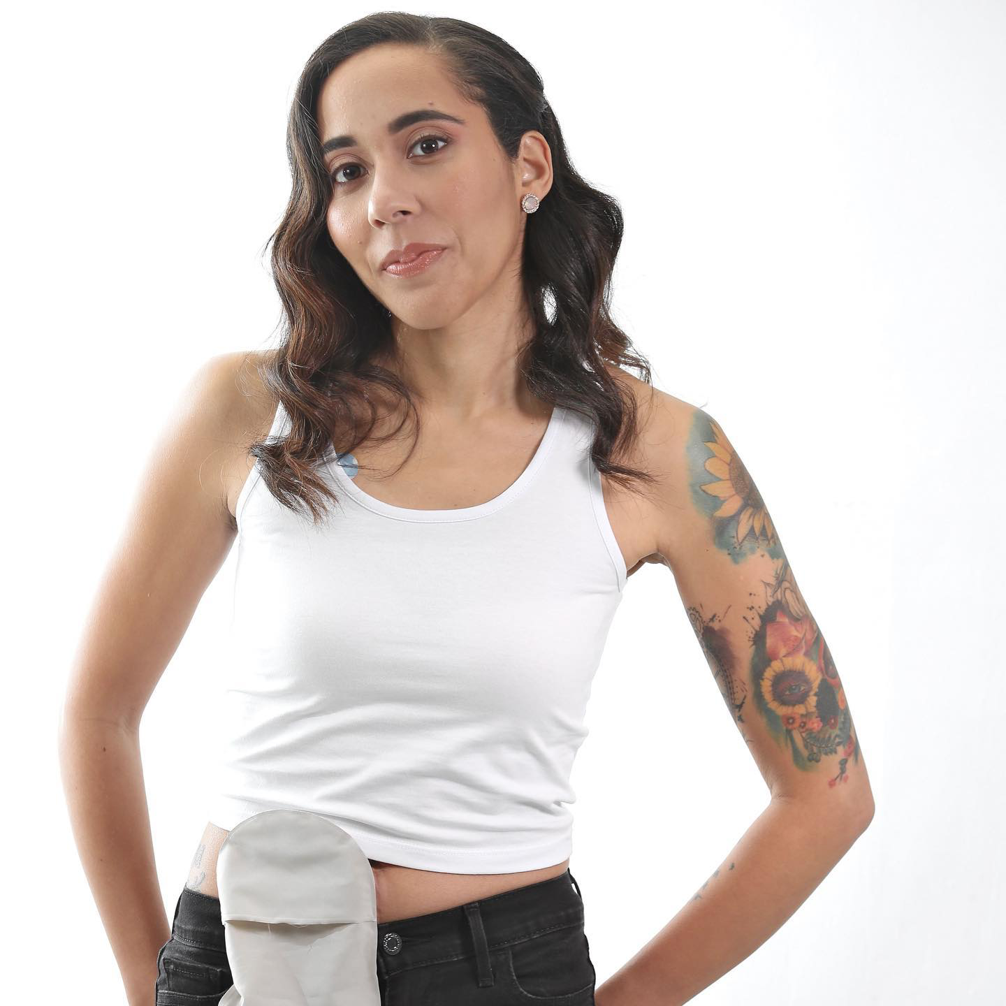 Keyla Ire poses proudly with her ostomy bag while wearing a white tank top.